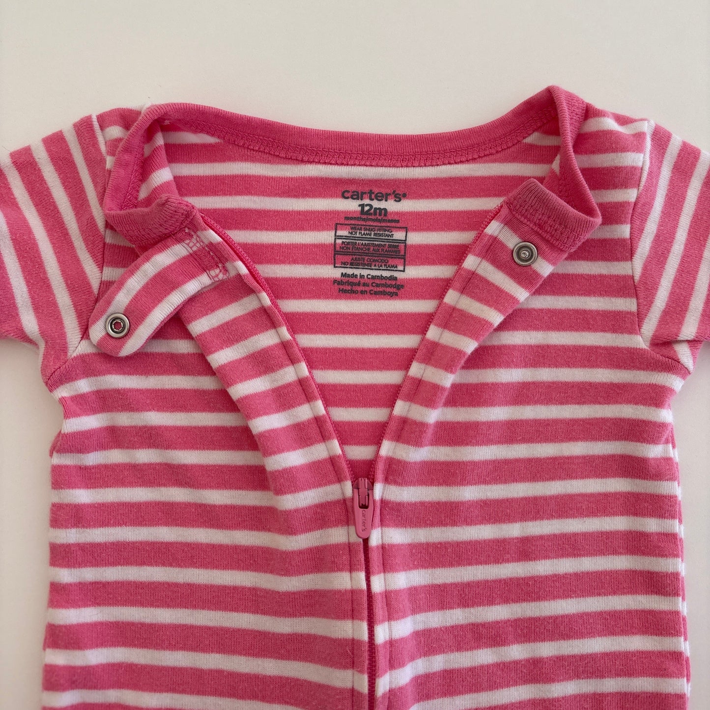 Pink and white striped baby onesie on a light beige background