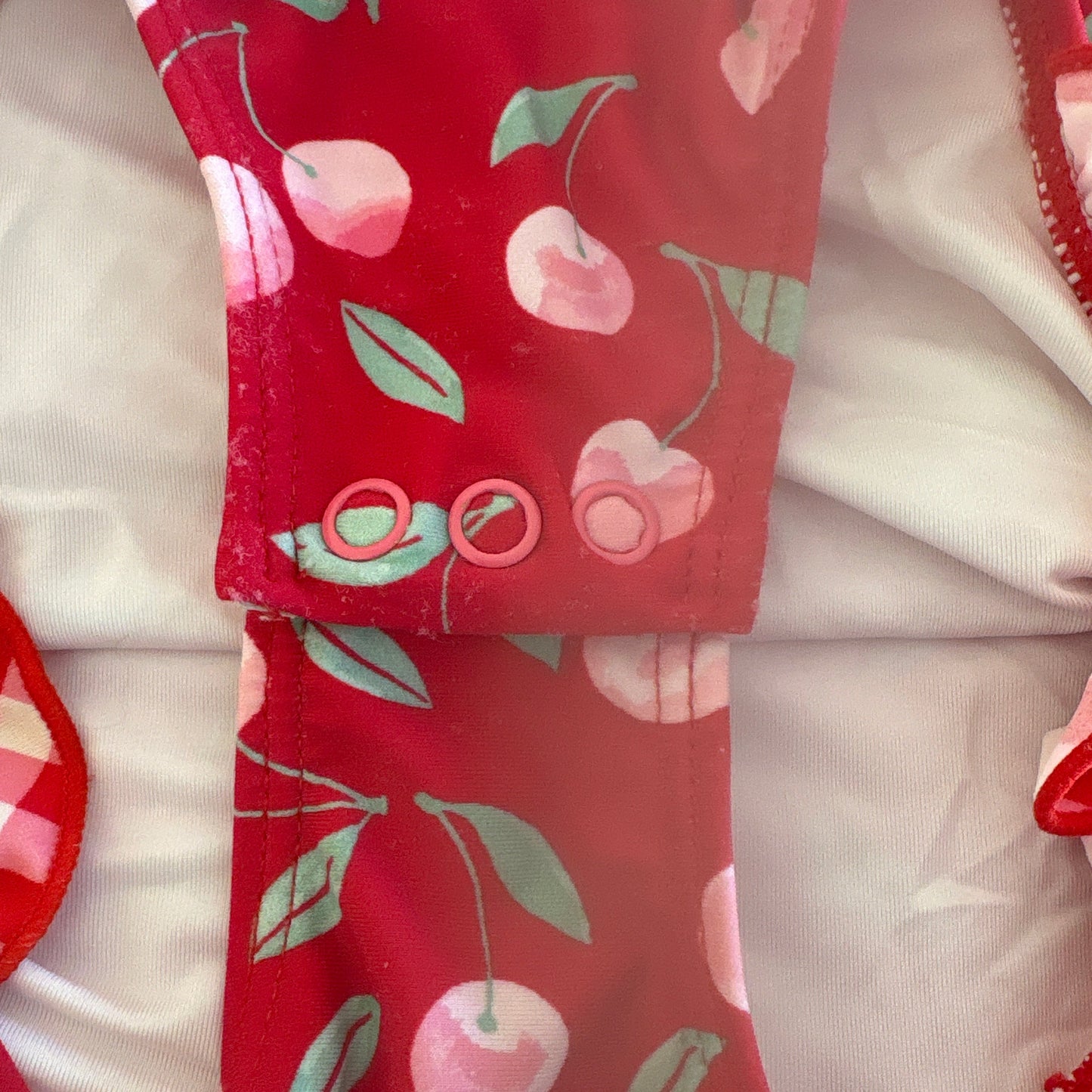 Red swimsuit with cherry pattern on a white background, shows small signs of wear on swimsuit bottom