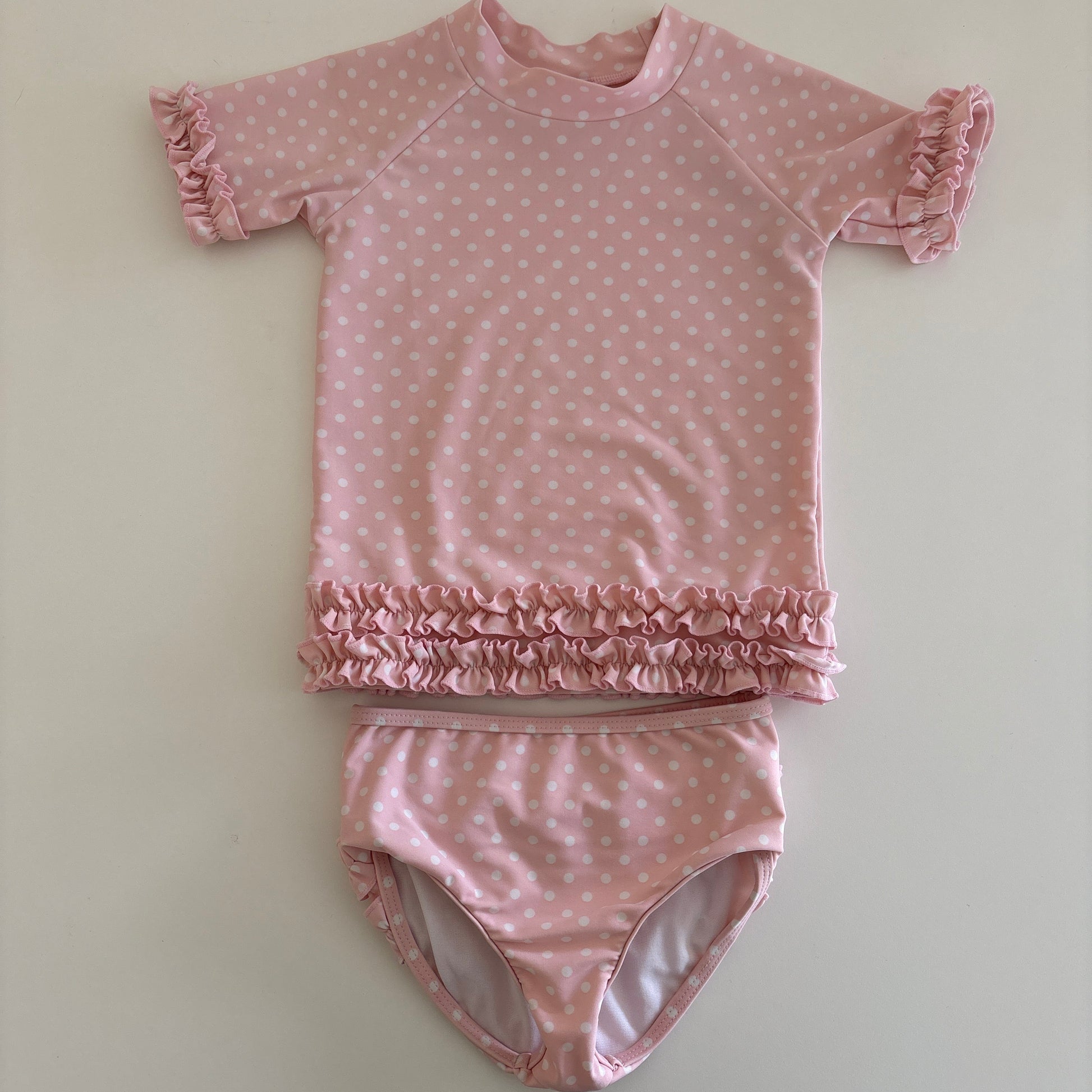 Pink polka dot baby swim outfit with ruffled details on a light background