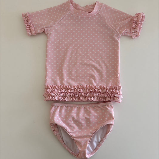 Pink polka dot baby swim outfit with ruffled details on a light background