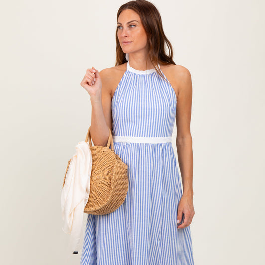 Woman wearing a blue and white striped dress holding a straw bag on a plain background