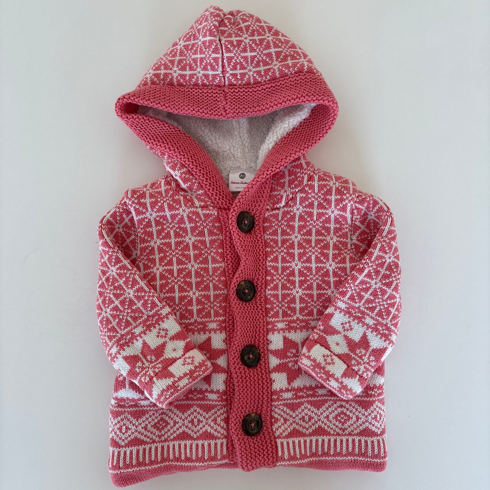 A small pink and white patterned knit pet sweater with a hood and snap buttons, laid flat on a white surface.