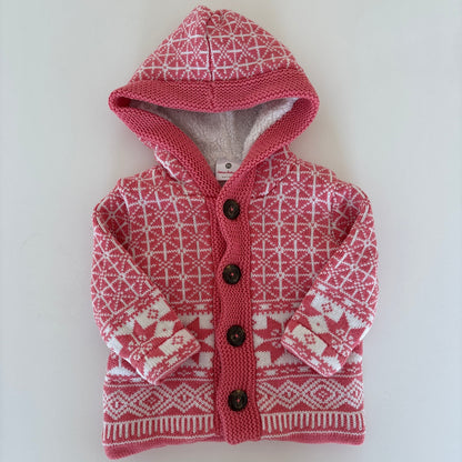 A small pink and white patterned knit pet sweater with a hood and snap buttons, laid flat on a white surface.