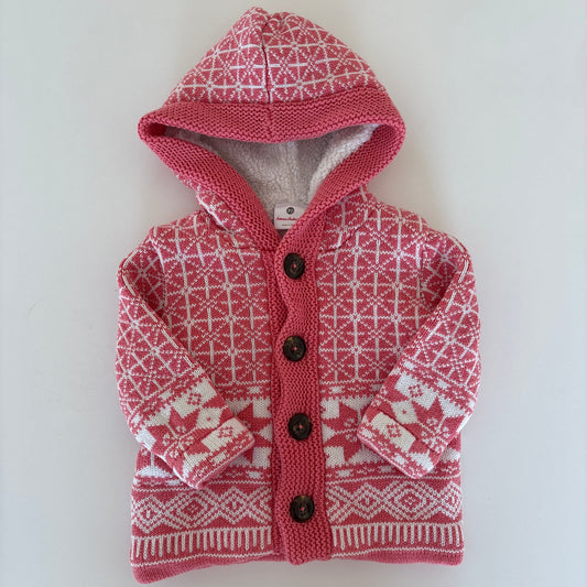 A small pink and white patterned knit pet sweater with a hood and snap buttons, laid flat on a white surface.