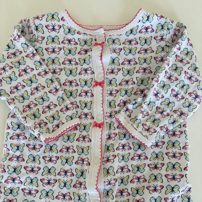 A close-up of a white fabric garment or textile with an allover butterfly print in pink, blue, and yellow, featuring a decorative pink stitched trim.