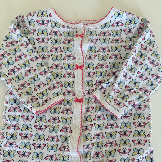 A close-up of a white fabric garment or textile with an allover butterfly print in pink, blue, and yellow, featuring a decorative pink stitched trim.