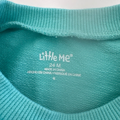 Close-up of a teal fabric with 'Little Me' branding on a light background