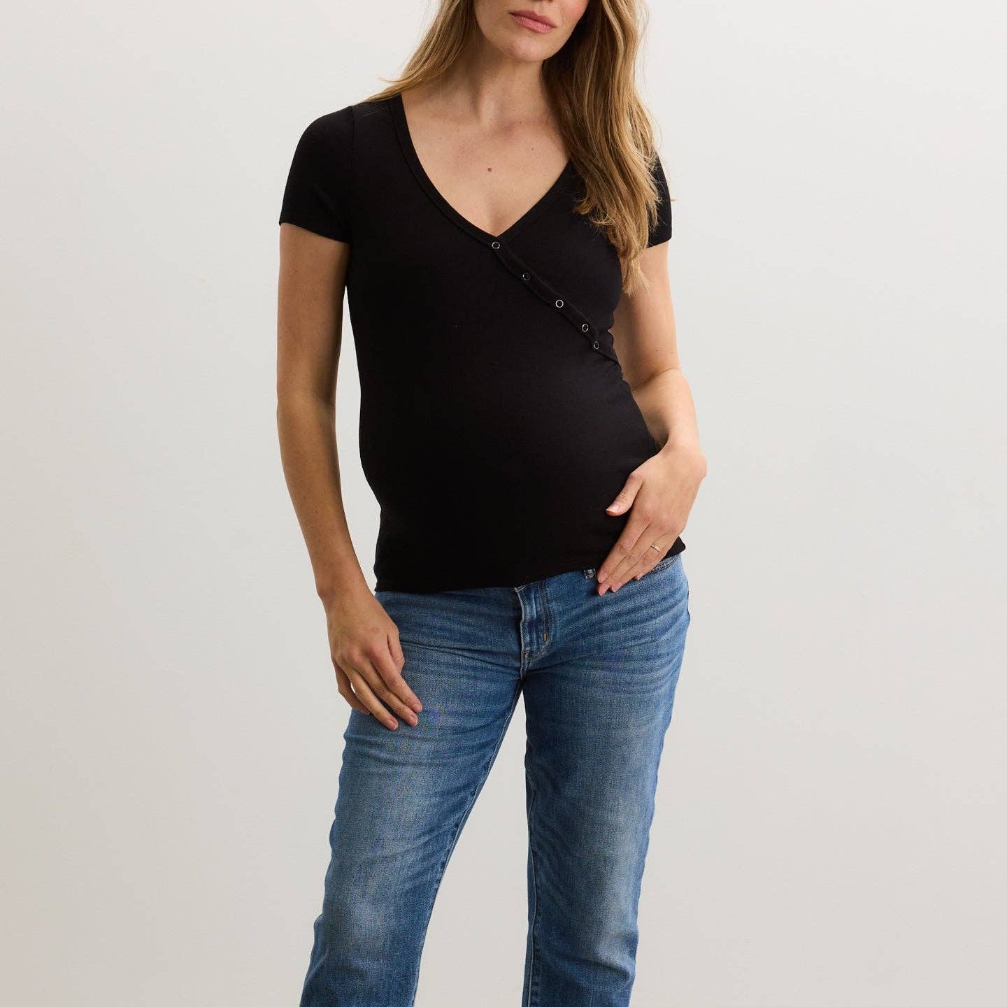 Woman wearing a black top and blue jeans against a plain background