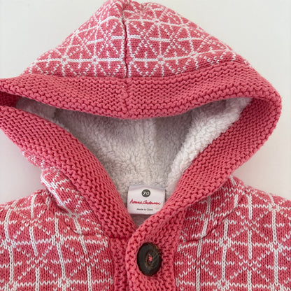 A close-up of a pink and white patterned knit pet coat with a soft white fleece lining and one dark brown buttons.