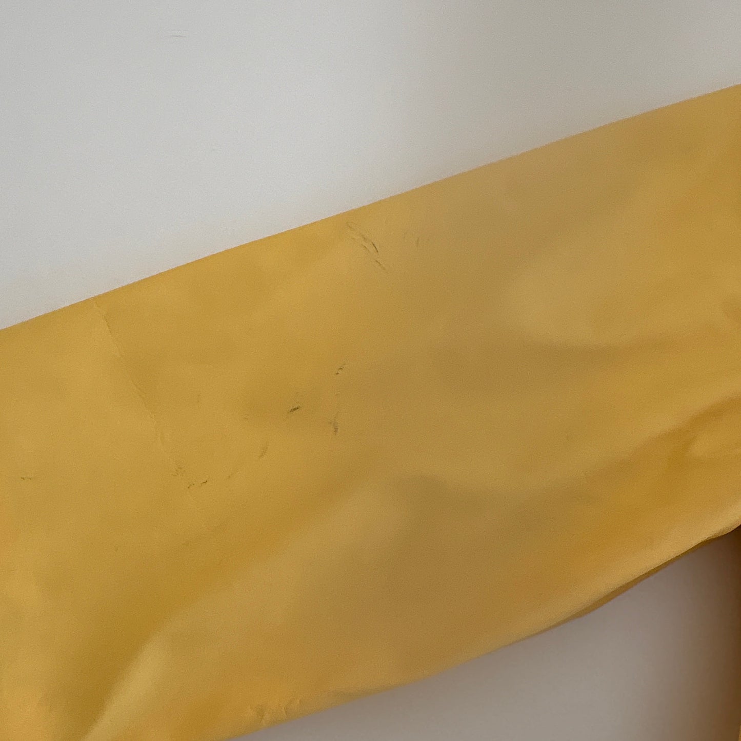 Yellow fabric on a white background, shows some markings on the sleeve of the raincoat