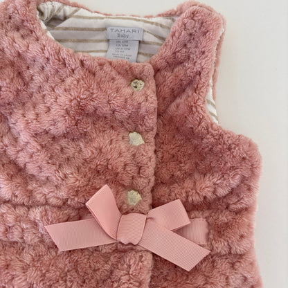 A close-up of a pink fuzzy textured vest with a matching pink ribbon bow at the center front, featuring three decorative buttons and a striped lining visible inside the collar. The brand label reads TAHARI.