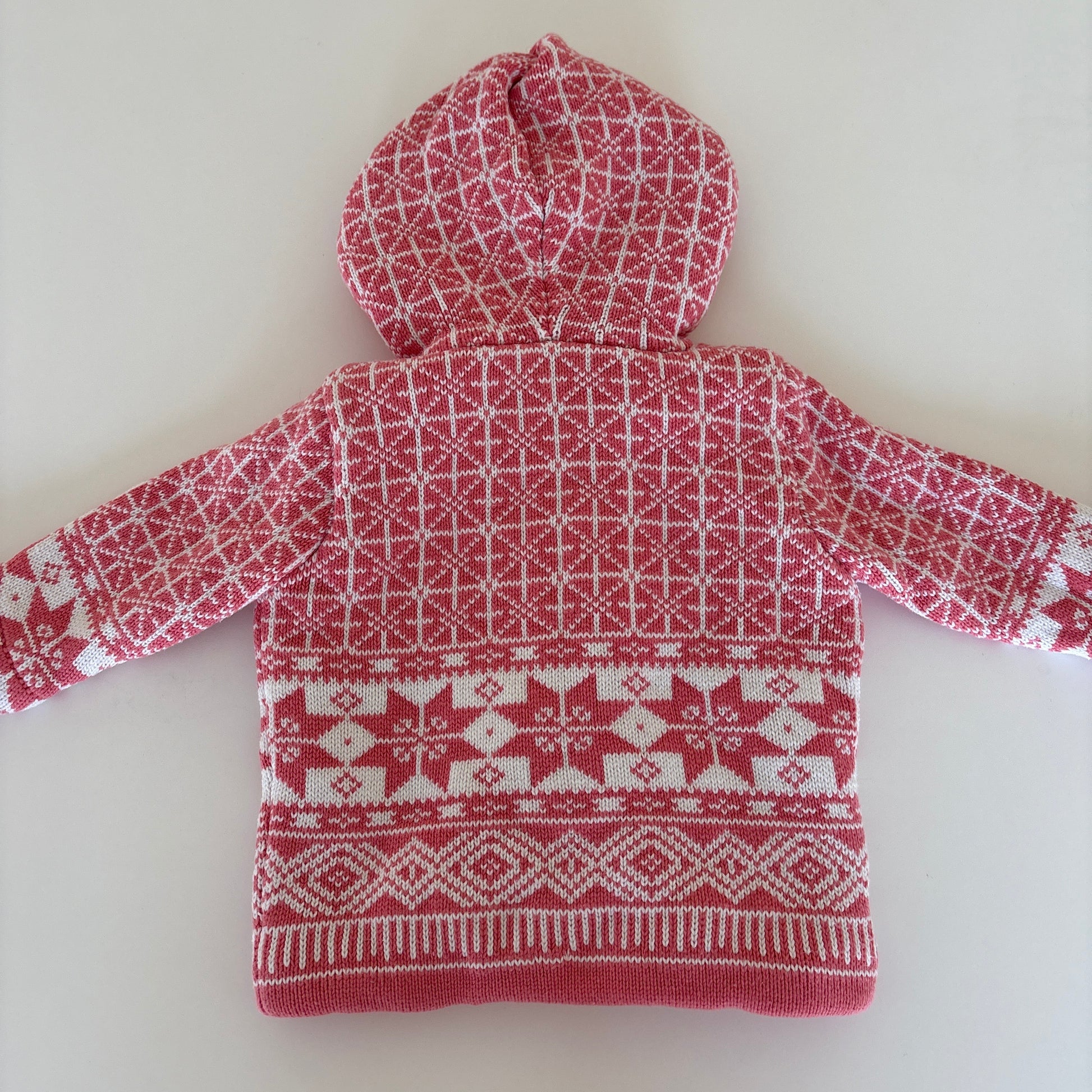 A pink and white patterned knit hooded sweater laid flat on a light off-white background.