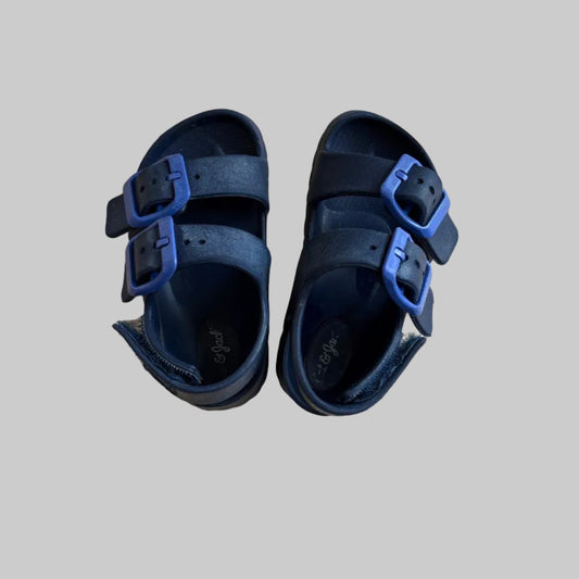 Pair of navy sandals with blue buckles on a gray background