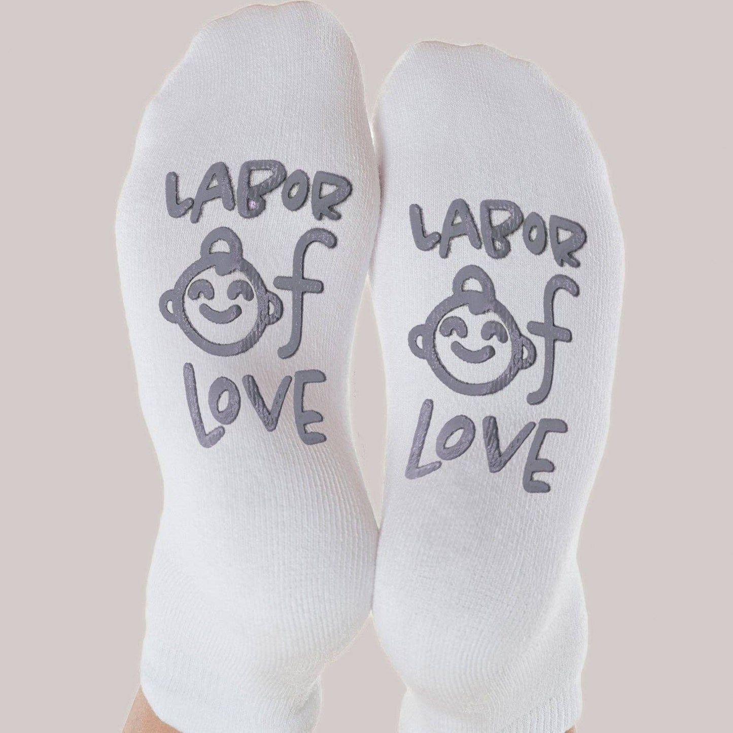 White socks with 'Labor of Love' text and baby illustration on a beige background