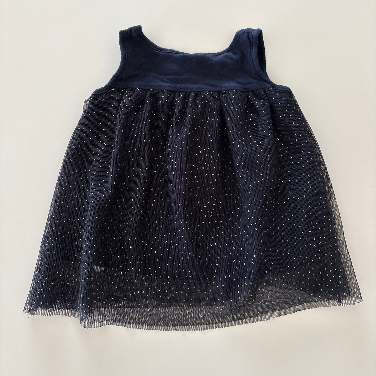 A sleeveless navy blue dress with a sheer tulle skirt featuring small glittery polka dots, laid flat on a light off-white background.