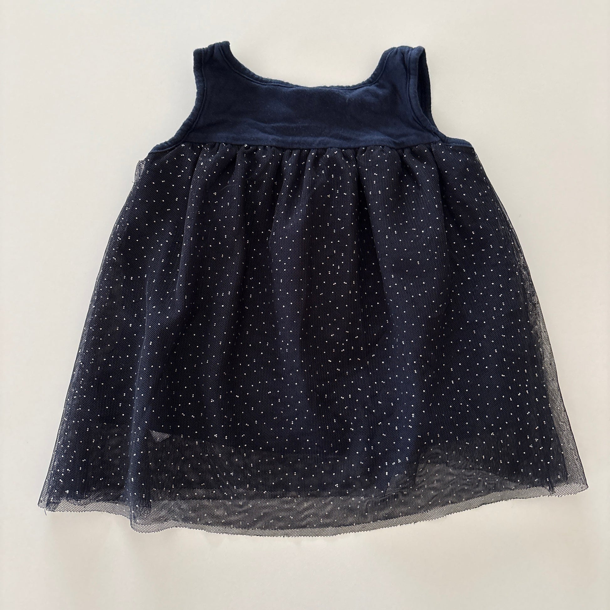 A sleeveless navy blue dress with a sheer tulle skirt featuring small glittery polka dots, laid flat on a light off-white background.