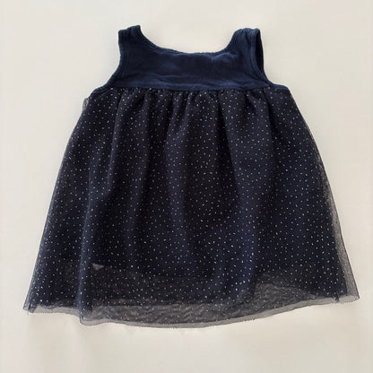 A sleeveless navy blue dress with a sheer tulle skirt featuring small glittery polka dots, laid flat on a light off-white background.