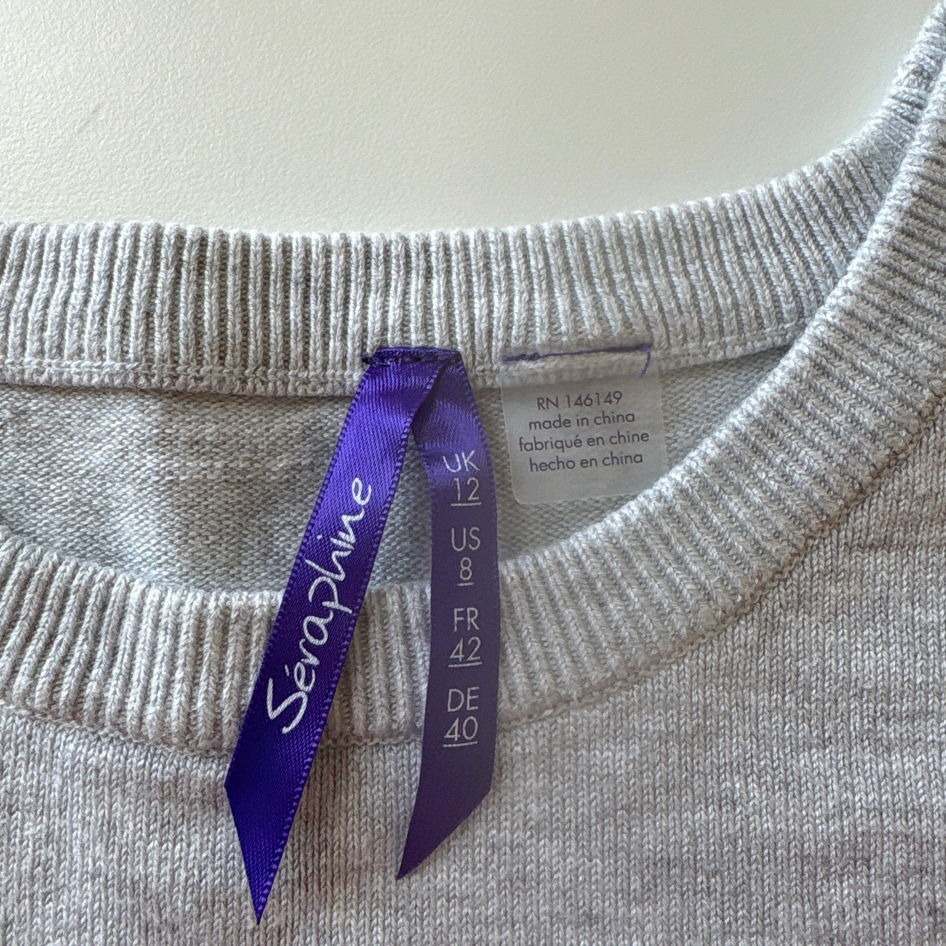 Gray sweater with a purple tag on a light gray background