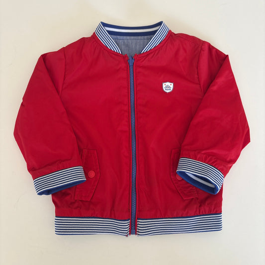 A red zip-up jacket with blue and white striped ribbed cuffs and collar, laid flat on a light beige background.
