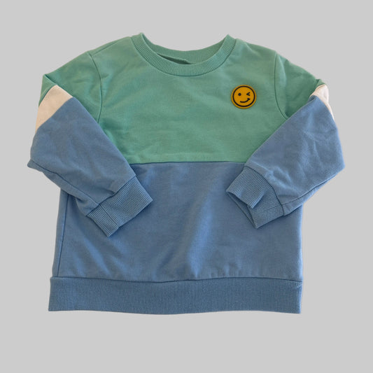 Green and blue children's outfit with a smiley face on a beige background