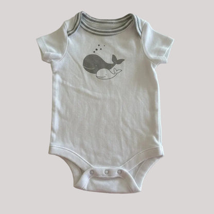 White baby onesie with a whale design on a beige background