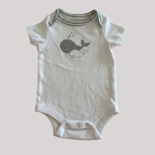 White baby onesie with a whale design on a beige background