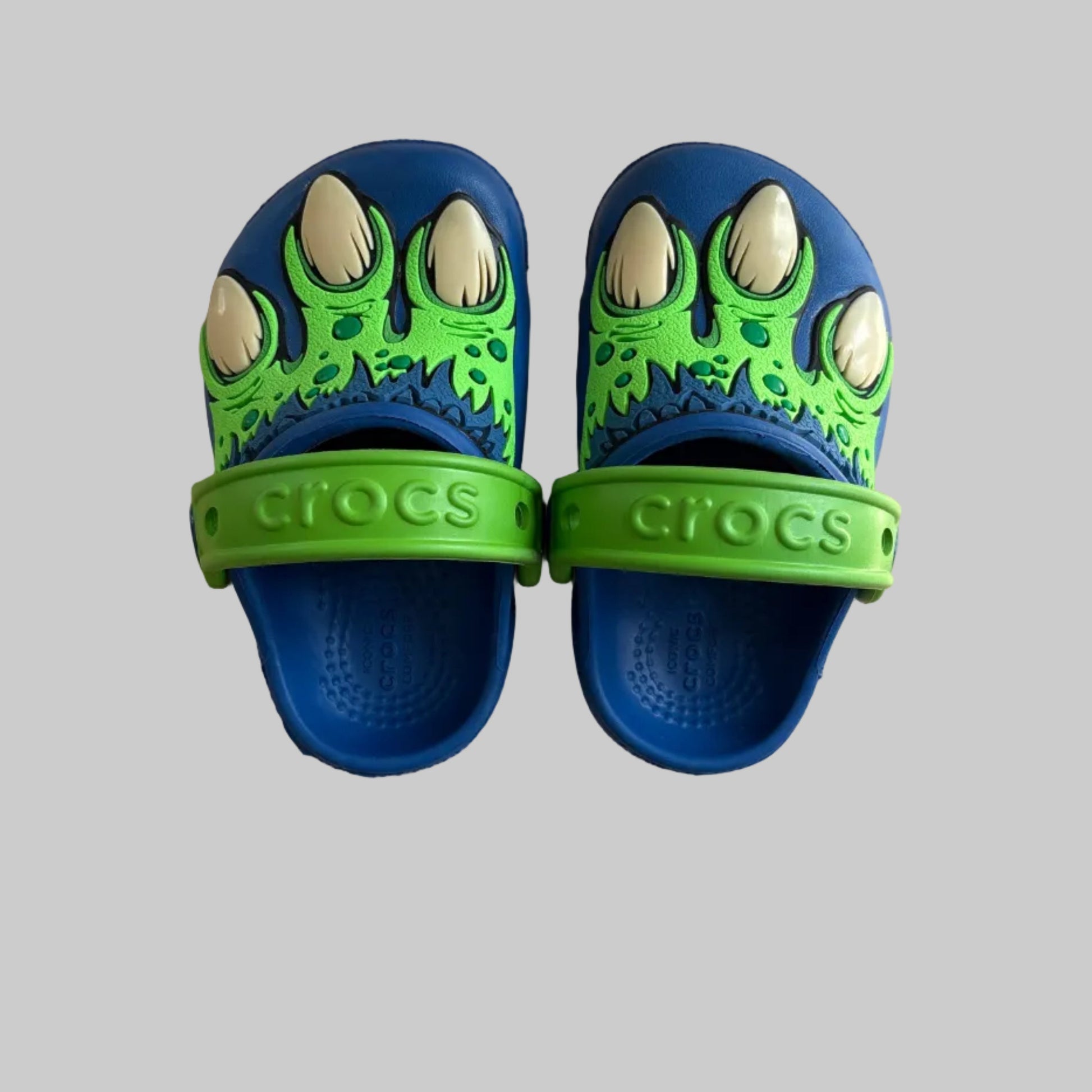 Pair of blue and green Crocs sandals on a gray surface