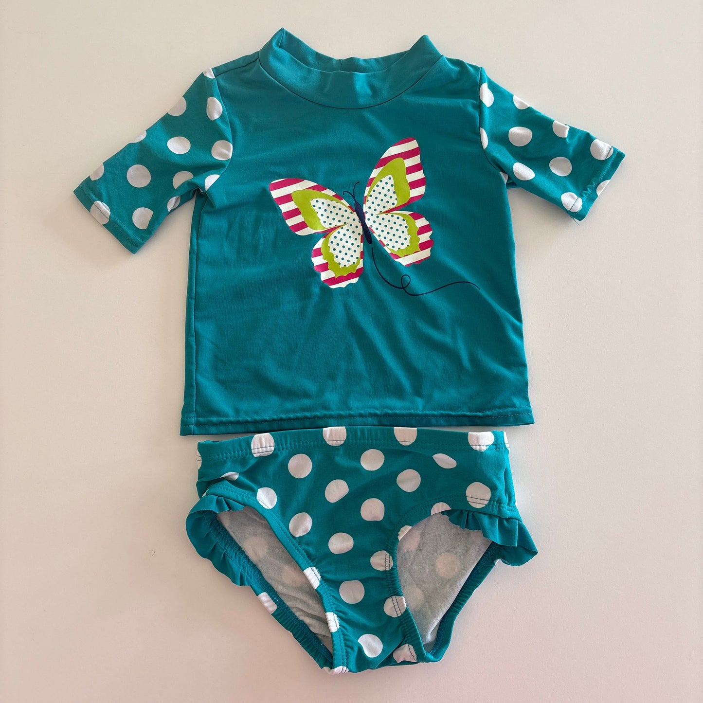 Teal children's swimsuit with polka dot pattern on a beige background