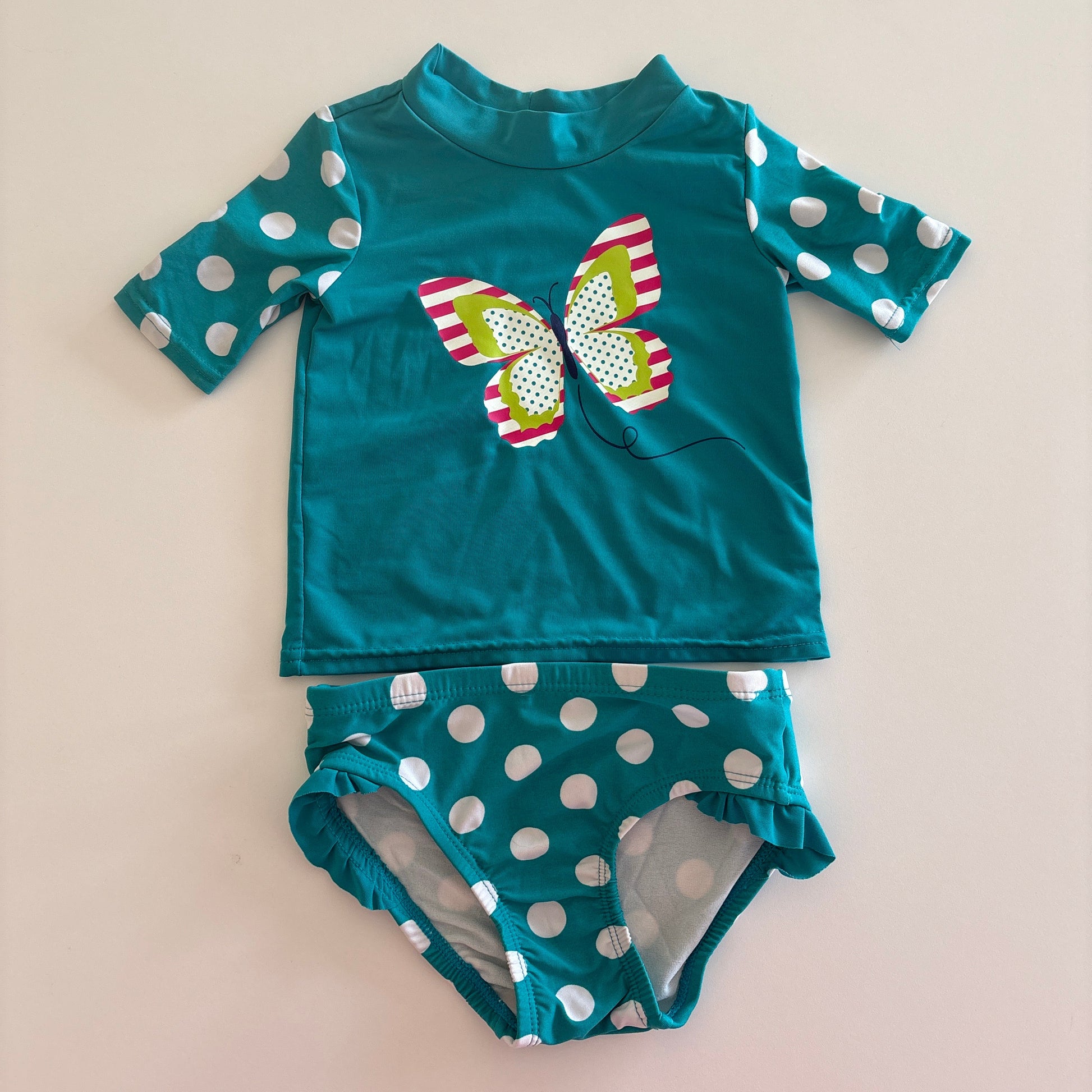 Teal children's swimsuit with polka dot pattern on a beige background