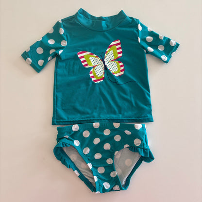 Teal children's swimsuit with polka dot pattern on a beige background