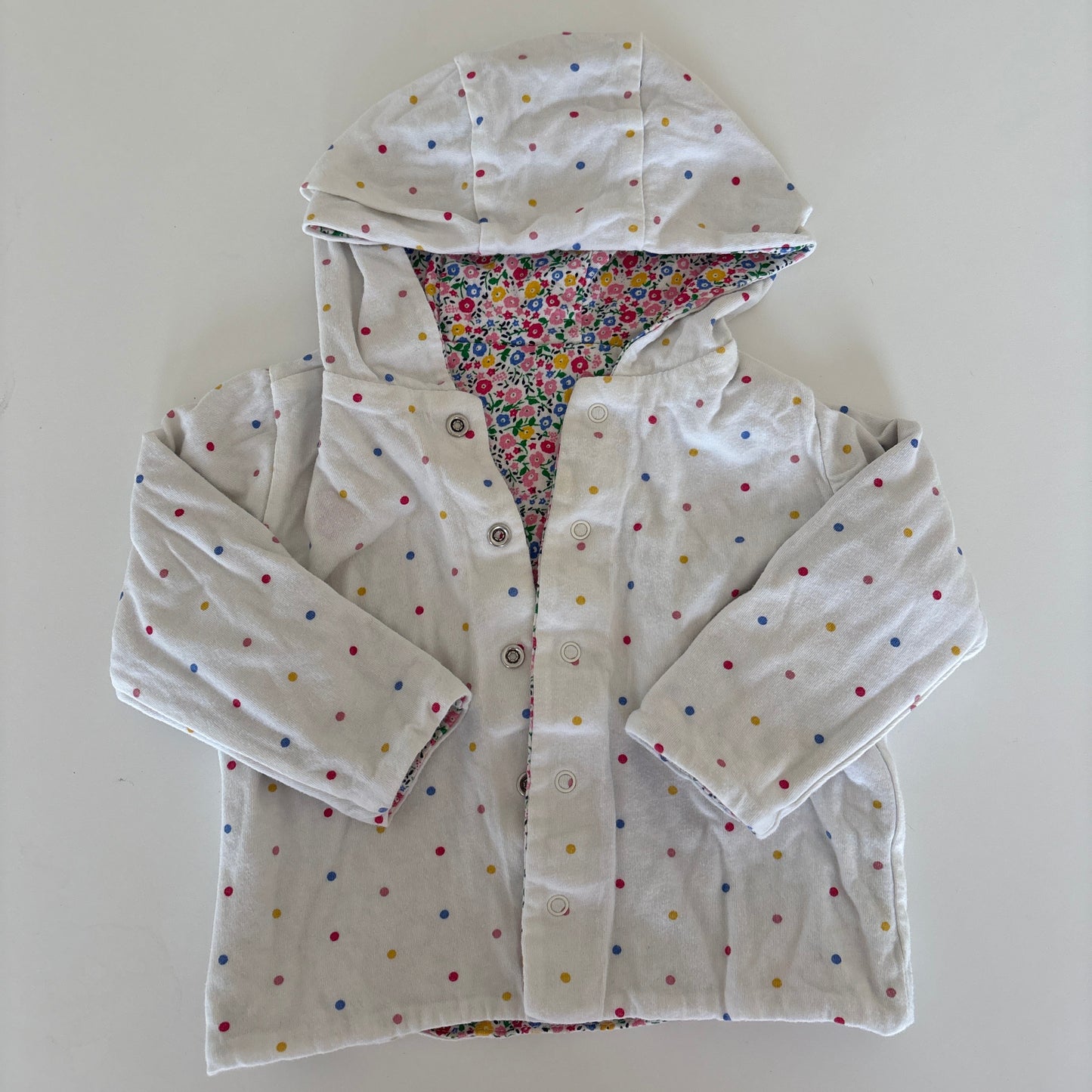 A white hooded jacket with small multicolored polka dots and a colorful patterned lining, laid flat on a white background.