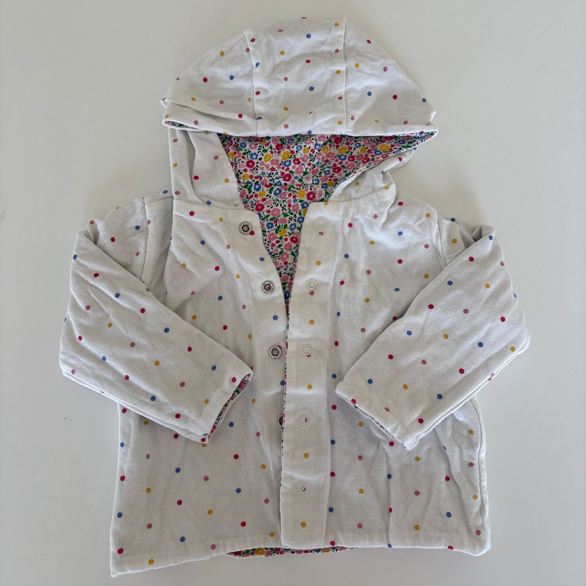 A white hooded jacket with small multicolored polka dots and a colorful patterned lining, laid flat on a white background.