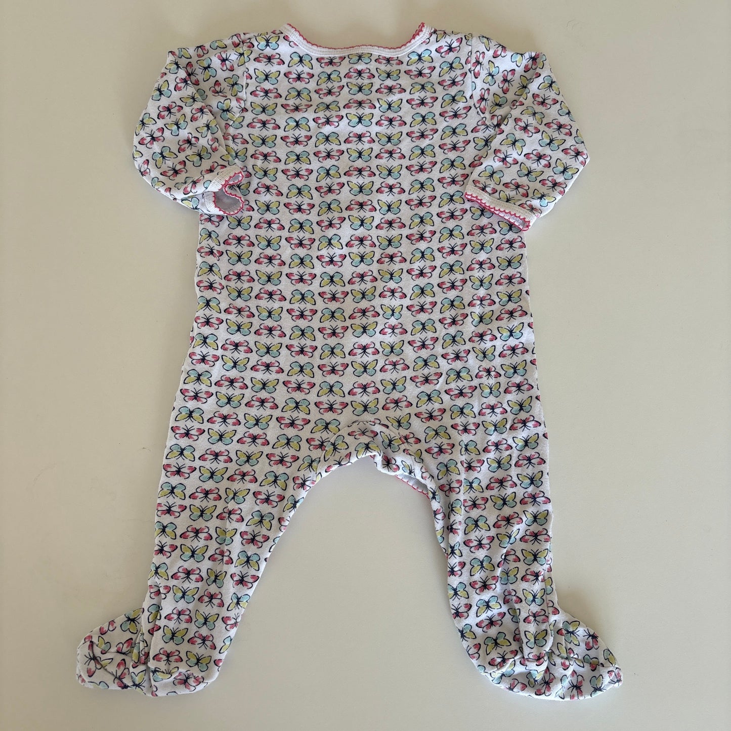 A baby long-sleeve footed sleeper with a dense butterfly print on a white background, laid flat on a beige surface.