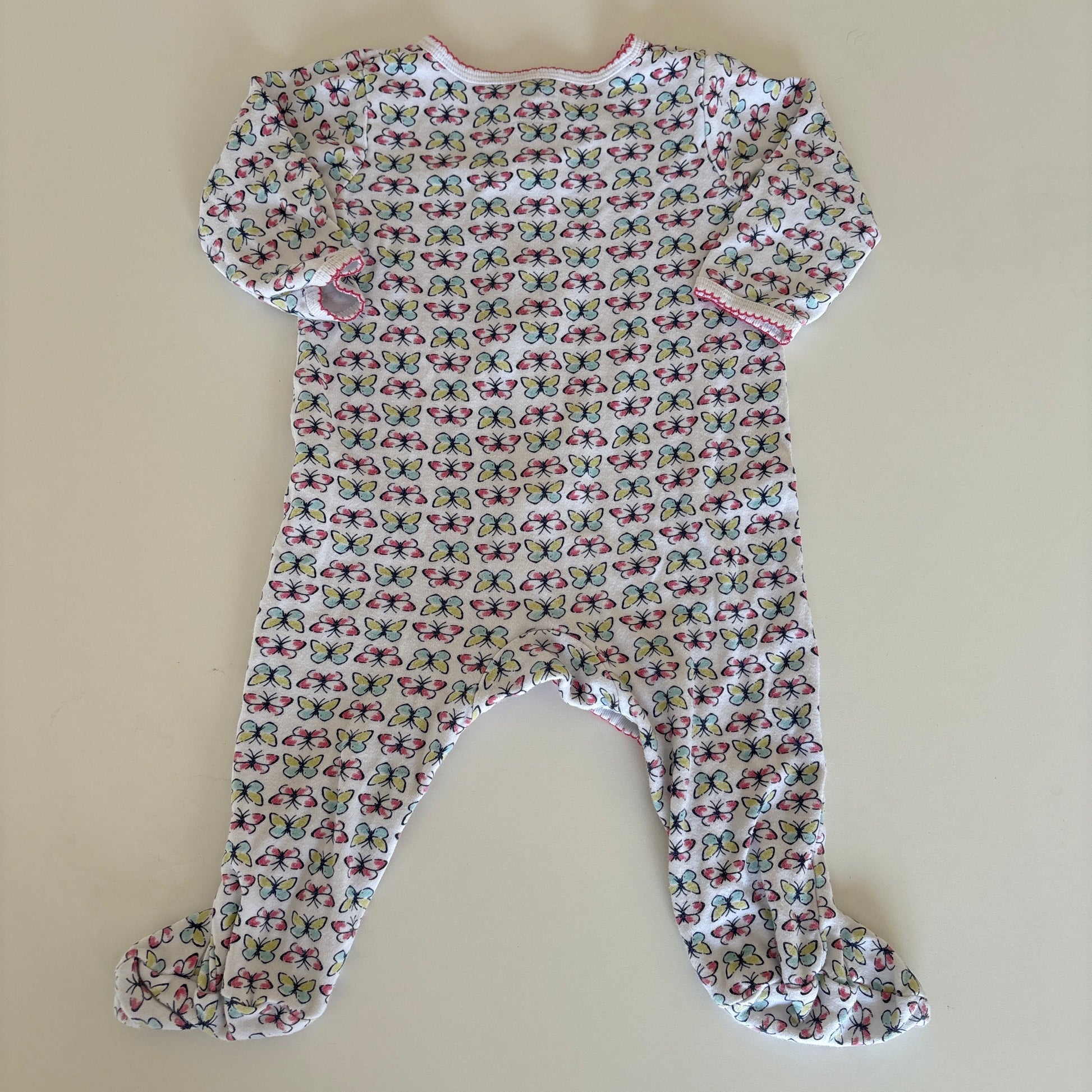 A baby long-sleeve footed sleeper with a dense butterfly print on a white background, laid flat on a beige surface.