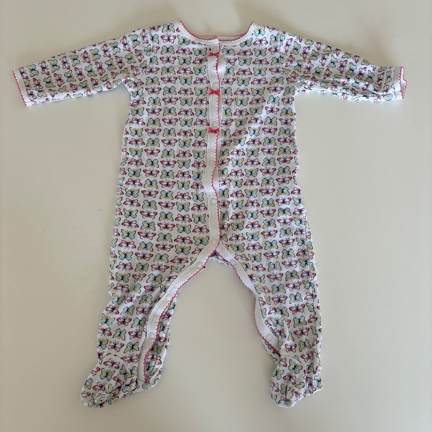 A baby long-sleeve footless romper with an all-over small floral print, laid flat on a light beige surface. The romper features a white base with a dense pattern of pink, red, and green butterflies, and has a snap closure at the chest.