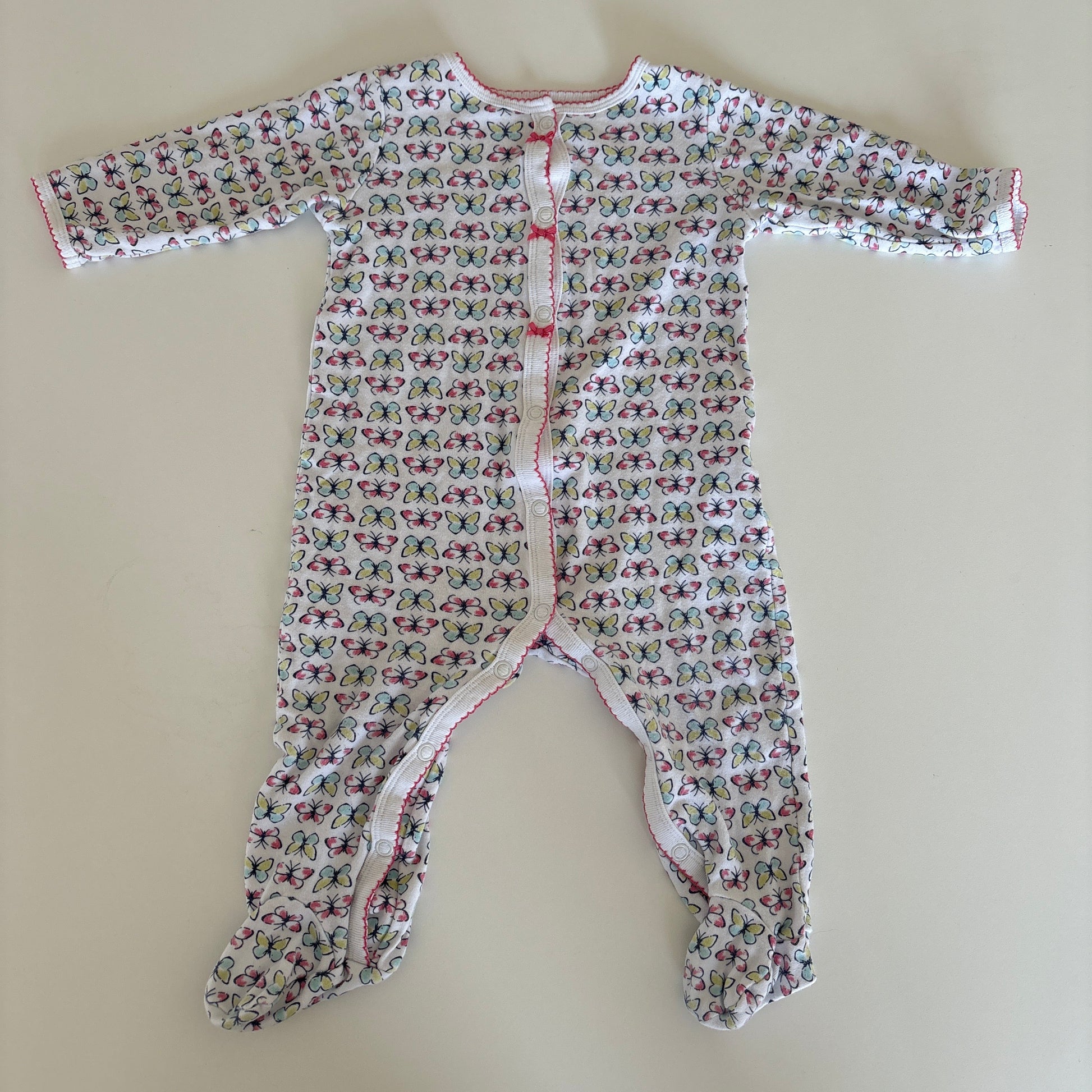 A baby long-sleeve footless romper with an all-over small floral print, laid flat on a light beige surface. The romper features a white base with a dense pattern of pink, red, and green butterflies, and has a snap closure at the chest.