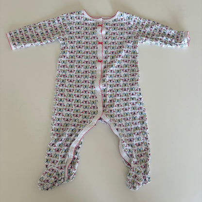 A baby long-sleeve footless romper with an all-over small floral print, laid flat on a light beige surface. The romper features a white base with a dense pattern of pink, red, and green butterflies, and has a snap closure at the chest.