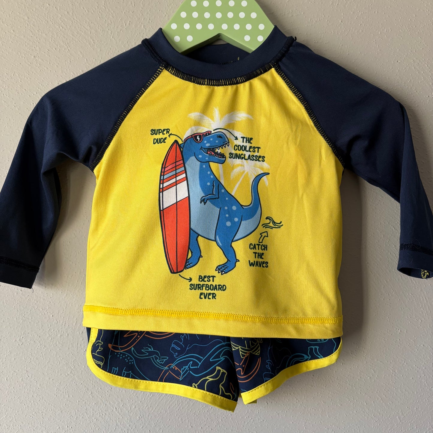 Children's swimsuit with dinosaur graphic on a hanger against a beige wall