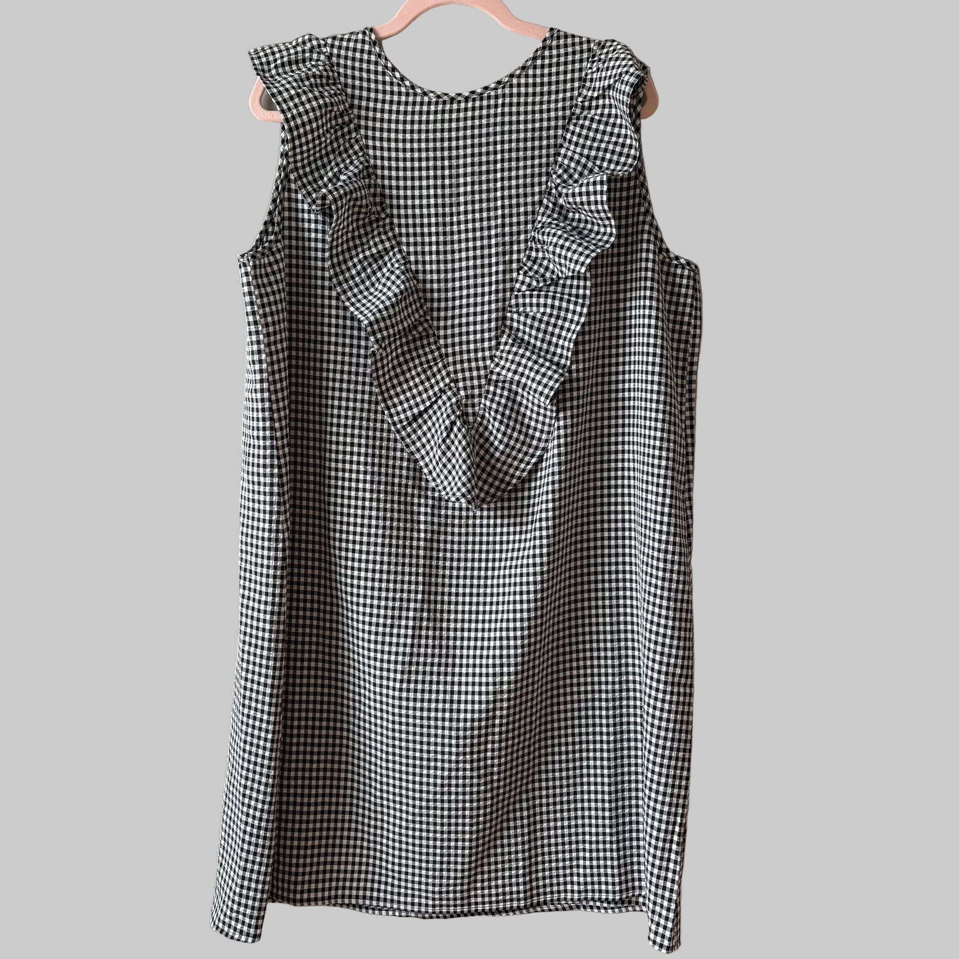 A sleeveless nursing dress in black and white gingham with a hidden zipper, displayed on a hanger