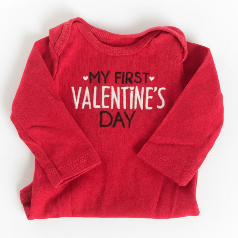 Red baby onesie with 'My First Valentine's Day' text on a textured surface