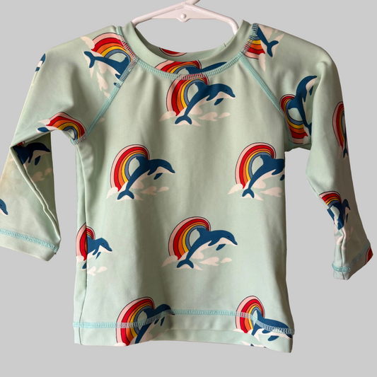Long sleeve swim shirt for toddlers with a pattern of dolphins and rainbows on a gray background, displayed on a hanger.