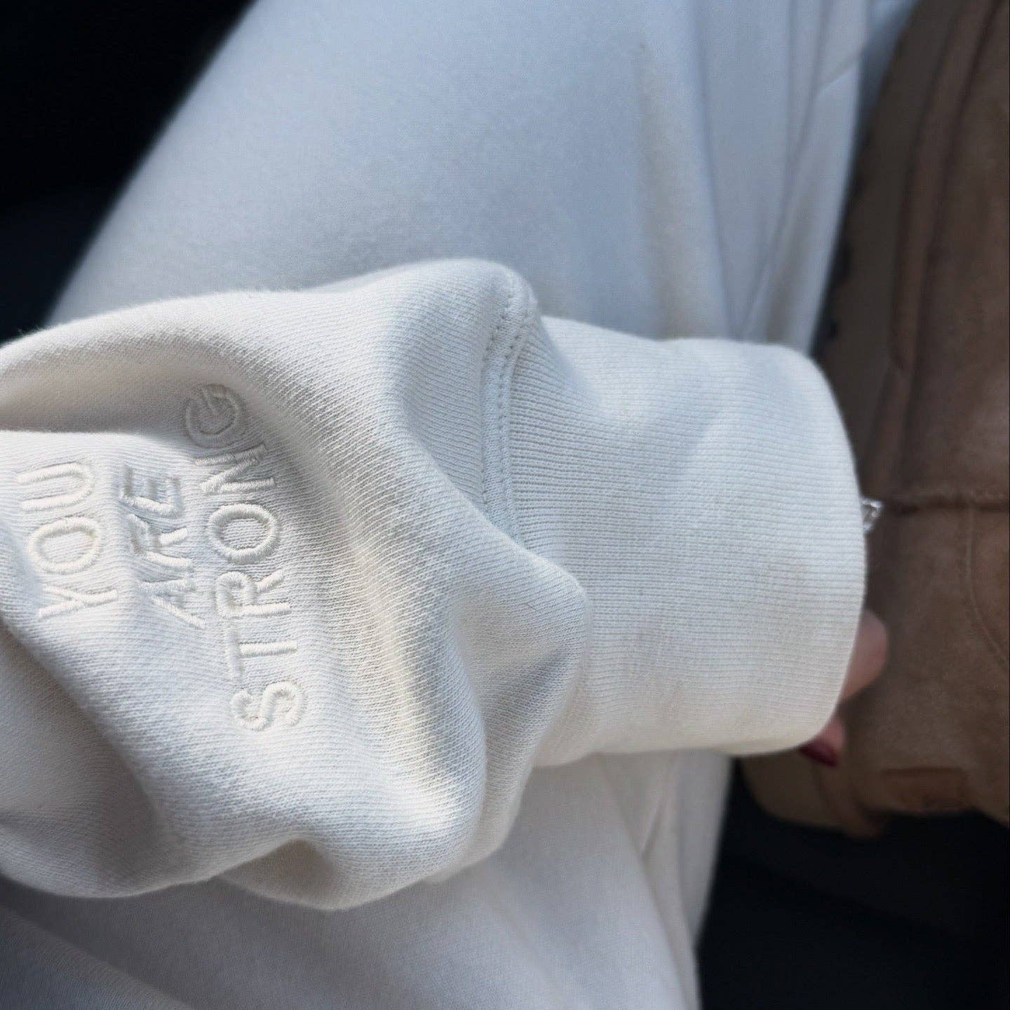 Close-up of a white sleeve with text that says you are strong on it, blurred background