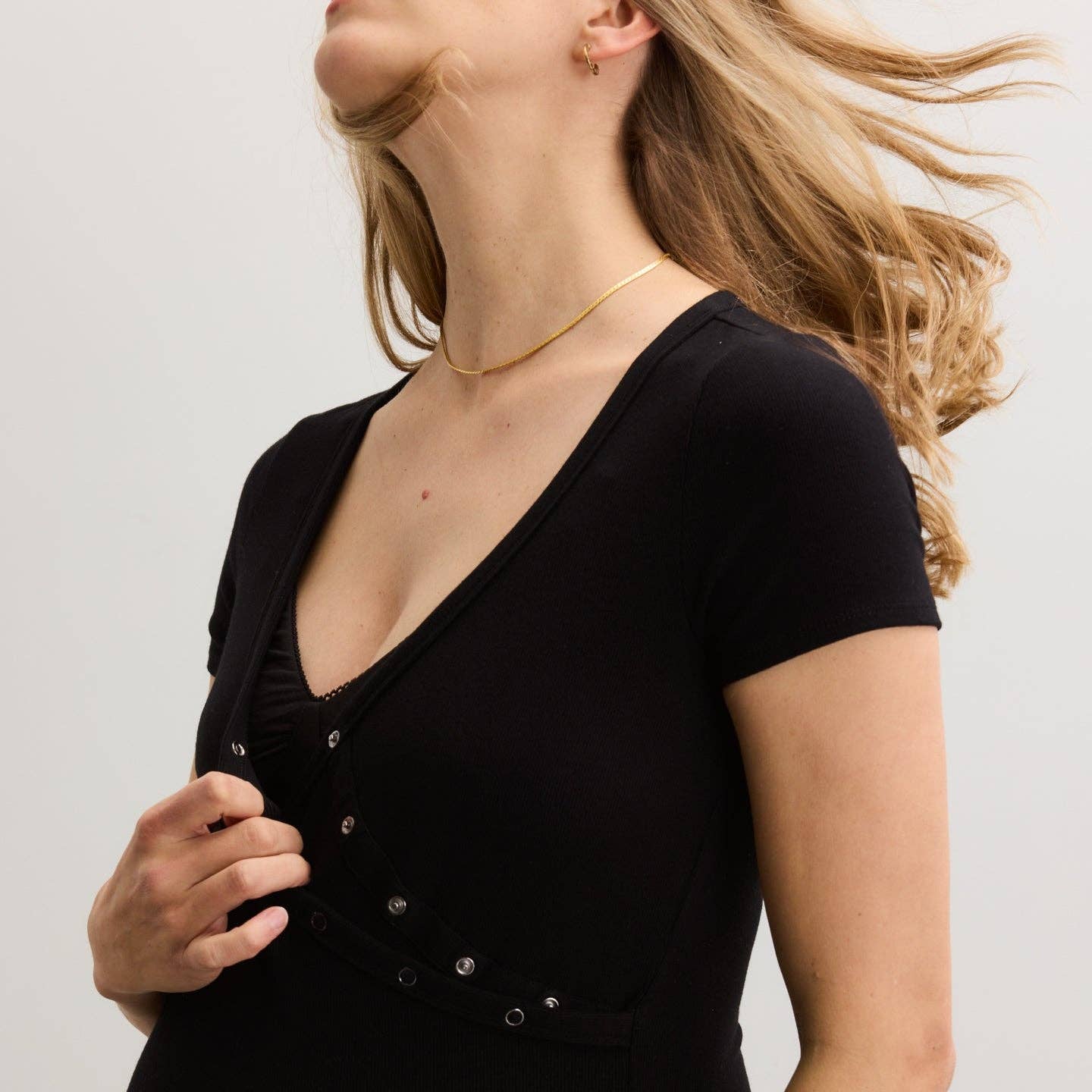 Woman wearing a black V-neck top with buttons on a plain background