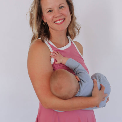 Woman in a pink nursing dress holding and breastfeeding a baby against a white background
