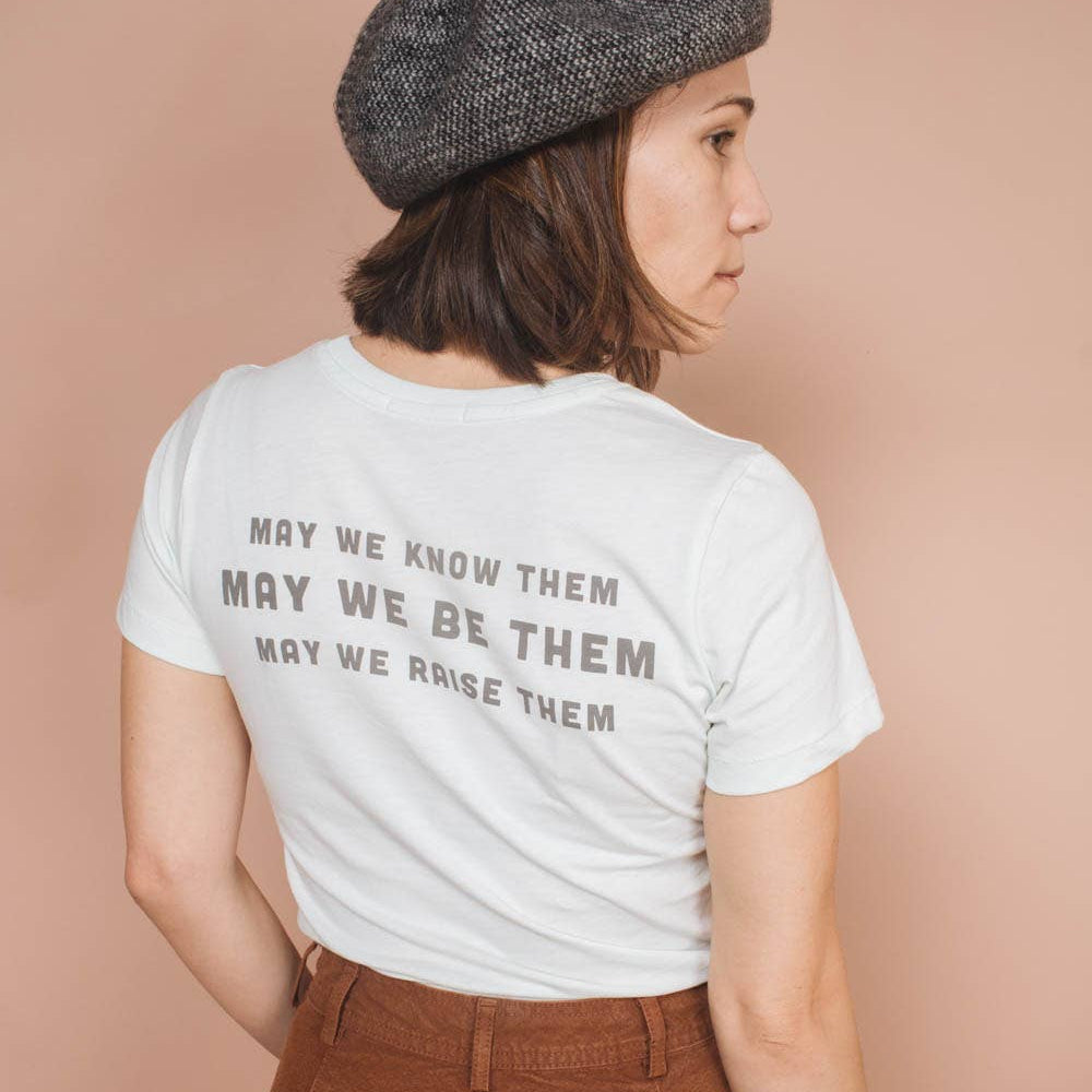 Person wearing a white t-shirt with text and a gray beret on a beige background