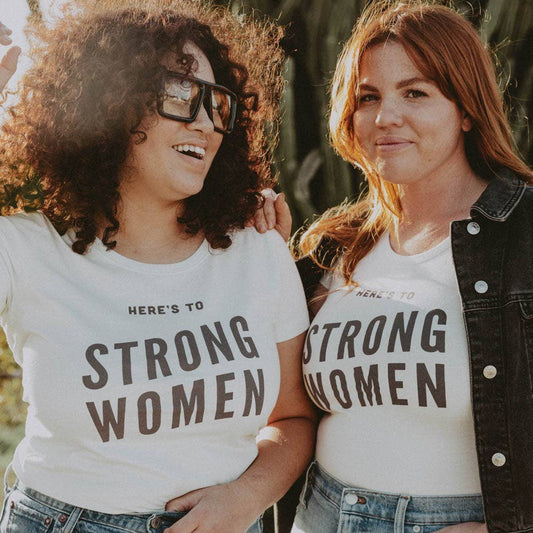 Two women wearing t-shirts with 'STRONG WOMEN' text, standing outdoors.