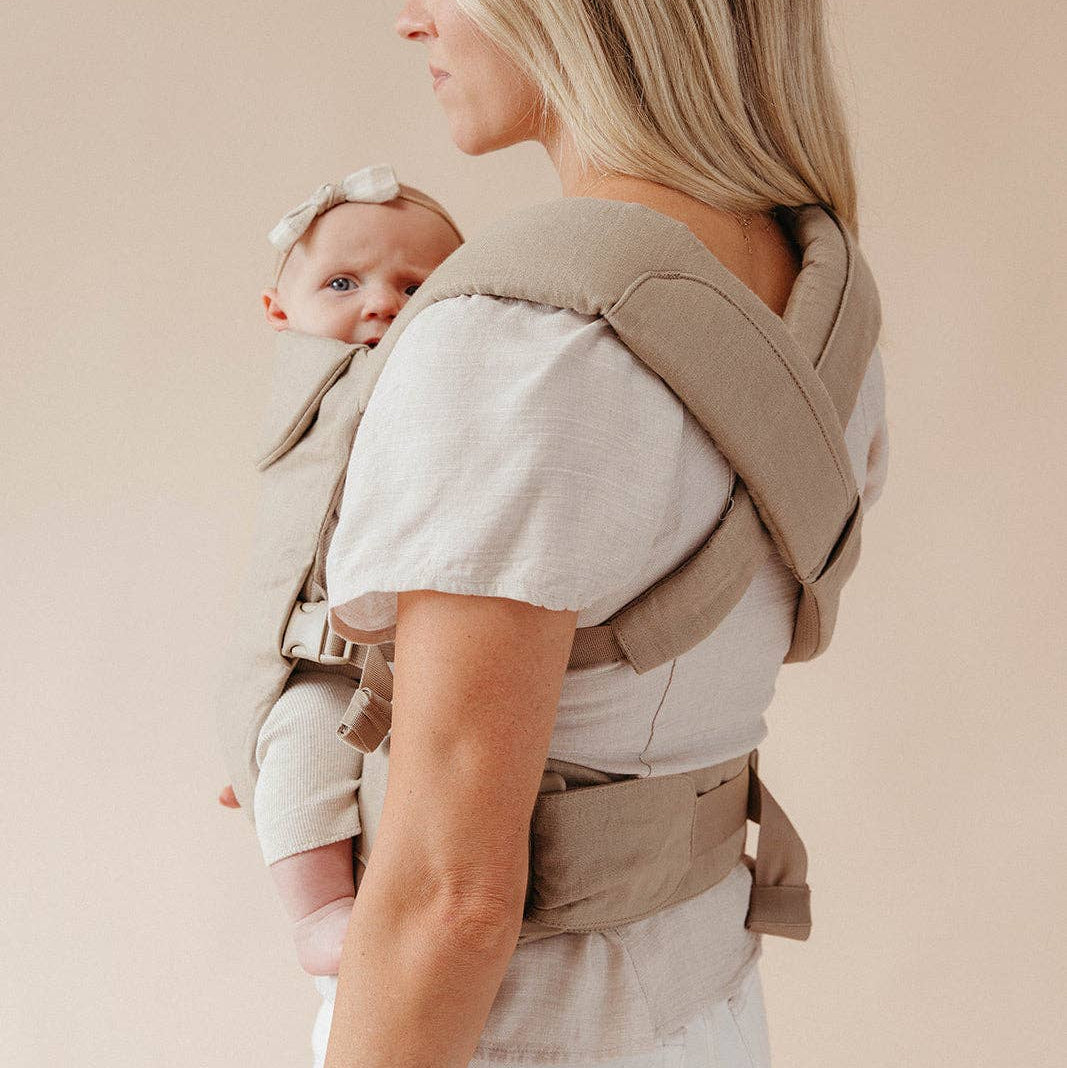 Woman carrying a baby in a beige baby carrier against a plain background