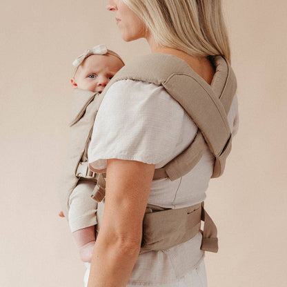 Woman carrying a baby in a beige baby carrier against a plain background