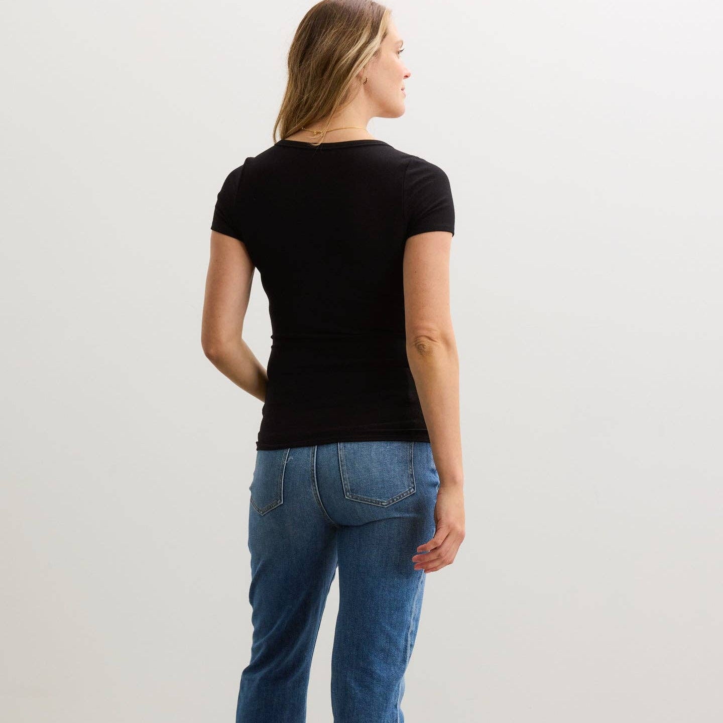 Person wearing a black t-shirt and blue jeans standing against a plain background