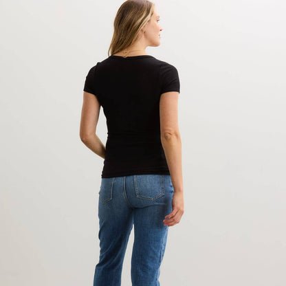 Person wearing a black t-shirt and blue jeans standing against a plain background
